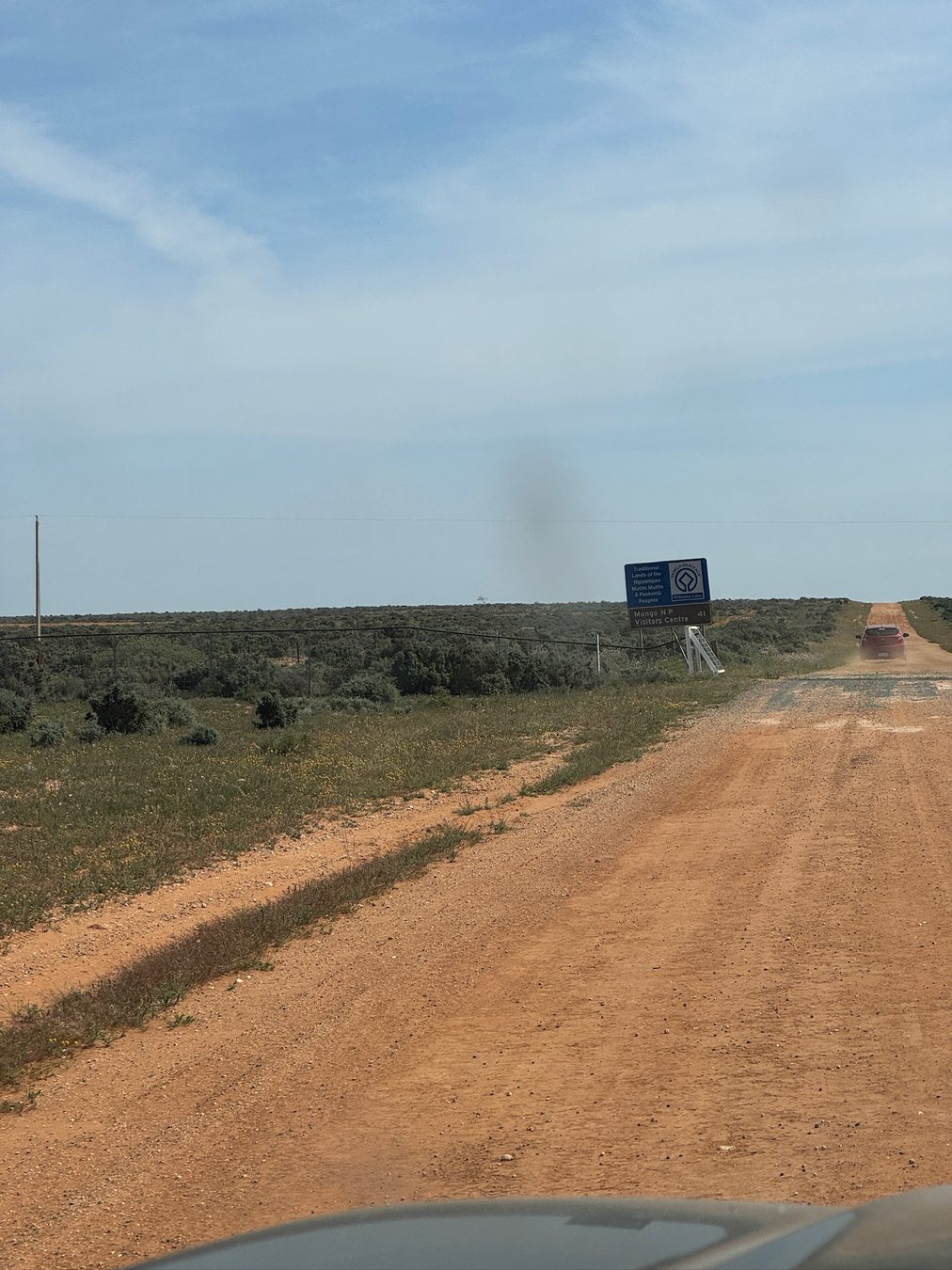 A straight red-dirt road crossing low outback scrub.