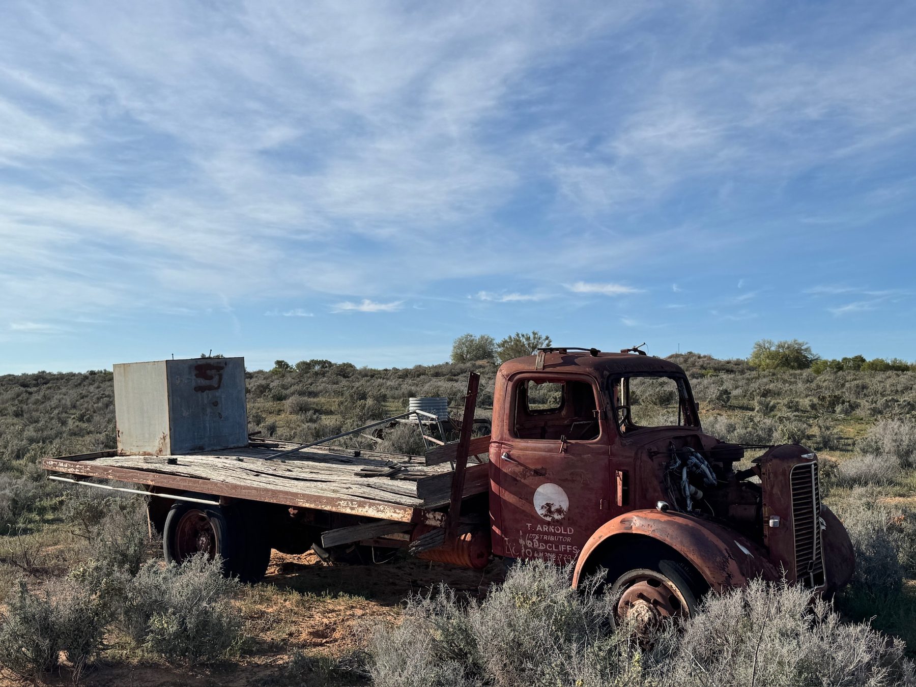 A side view of an abandoned red truck in the scrub.