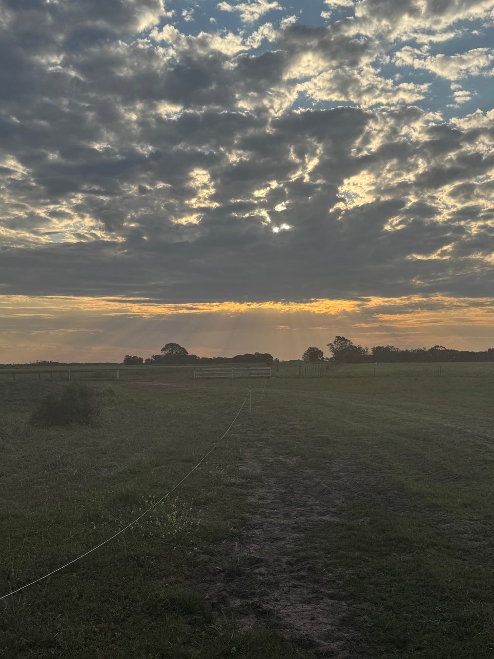 Sunset breaking through clouds over flat farm country.
